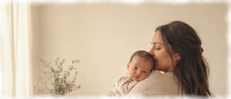 A mother kisses her newborn on the head.